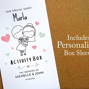 May include: A white rectangular box sleeve featuring a black line drawing of a couple embracing, surrounded by small pink and green hearts. Text reads: OUR SPECIAL GUEST Marla, ACTIVITY BOX, THE WEDDING OF MICHELLE & JOHN, and 01.08.2026.