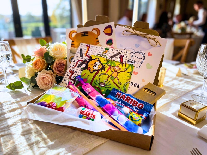 May include: A brown cardboard activity box containing a numbered game board, a colorful monkey-themed puzzle, a white activity book, a multi-colored silicone bubble fidget toy, a pack of Haribo Starmix, Love Hearts candy, and a small bag of dice.
