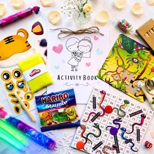 May include: A collection of children's activity items including a wedding-themed activity book, a jungle-themed jigsaw puzzle, a snakes and ladders board game, a pack of Haribo Starmix, a yellow Play-Doh container, glow sticks, and wooden pencils.