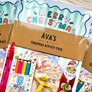 May include: Christmas activity packs with the words "Merry Christmas" and names on the front. Each pack contains a variety of colorful mini coloring pencils, a red bubble wand, and a yellow smiley face toy. The packs are wrapped in clear plastic.