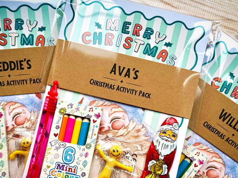 May include: Christmas activity packs with the words "Merry Christmas" and names on the front. Each pack contains a variety of colorful mini coloring pencils, a red bubble wand, and a yellow smiley face toy. The packs are wrapped in clear plastic.
