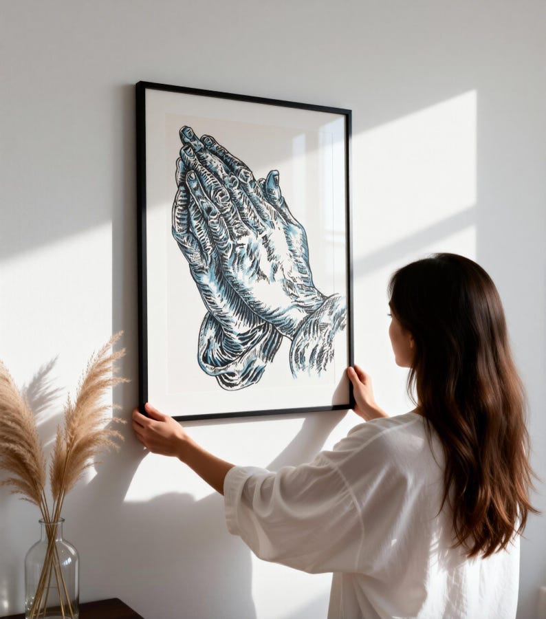 K&ouml;nnte beinhalten: Ein gerahmter Wandkunstdruck mit einer detaillierten Illustration von zwei in Gebetshaltung zusammengelegten H&auml;nden. Das Kunstwerk verwendet kr&auml;ftige schwarze Umrisse und blaue Schattierungen auf wei&szlig;em Grund in einem schwarzen Rahmen.