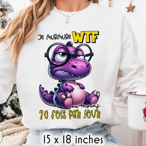 May include: White sweatshirt featuring a purple cartoon dinosaur wearing glasses. Text above reads "Je murmure WTF au moins 20 fois par jour." The design is 15 x 18 inches.