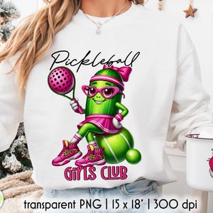 Op de afbeelding: Witte sweatshirt met een cartoon augurkenpersonage dat pickleball speelt. De augurk draagt een roze bril, een hoofdband en een rok, met de woorden "Pickleball Girls Club" in het roze. Het ontwerp bevat een pickleball-racket en -bal.