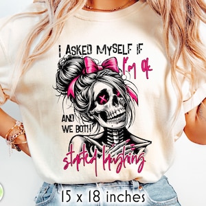 May include: Cream-colored t-shirt featuring a skull with a pink bow and the text "I asked myself if I'm ok and we both started laughing." The shirt measures 15 x 18 inches.
