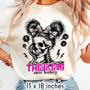 May include: Cream-colored t-shirt featuring a black and white skull design with bows in its hair and a skeleton torso. The text "THINKING about thinking" is in pink. The shirt measures 15 x 18 inches.