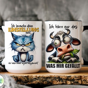 May include: Two white ceramic mugs with black handles and rims. One mug features a grumpy blue cat illustration with German text. The other mug has a cow wearing glasses and eating grass, also with German text. Both mugs have text.