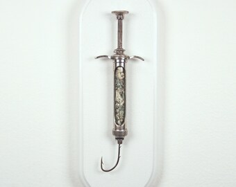 Hooked V5 - Satirical dollar bill/fishook/syringe sculpture from Nemo Gould