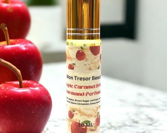 Può includere: Un flacone da 10 ml di profumo gourmand alla mela e caramello. Il flacone è dorato e presenta un'etichetta con la scritta "Mon Tresor Beaut" e un design a mela rossa.