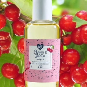 Op de afbeelding: Een heldere glazen fles body oil met een witte dop. Het roze etiket leest "Cherries & Stilettos Body Oil" met een kersenillustratie. De achtergrond toont rode kersen en groene bladeren. De fles bevat 59 ml olie.