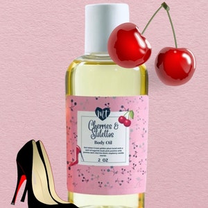 Op de afbeelding: Een flesje lichaamsolie met het label "Cherries & Stilettos". Het label is roze met een kersendesign. Een paar zwarte hoge hakken met rode zolen en twee rode kersen staan ook in de afbeelding. De fles bevat 59 ml olie.