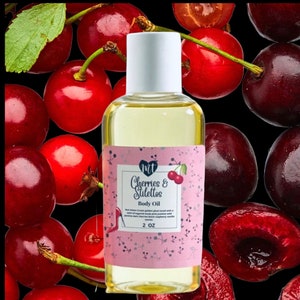 Op de afbeelding: Een heldere glazen fles body oil met een witte dop, met het label "Cherries & Stilettos". Het label is roze met een kersenillustratie. De achtergrond is een zwart oppervlak bedekt met verse rode kersen.