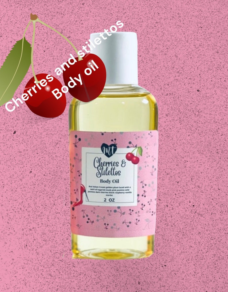 Op de afbeelding: Een kleine fles heldere body oil met een witte dop. Het etiket toont "Cherries & Stilettos Body Oil" met een kersen- en stiletto-afbeelding. De fles is 59 ml en staat tegen een roze achtergrond.