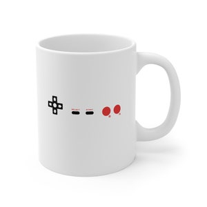 May include: White ceramic mug with a black and red video game controller design. The design features a directional pad, two buttons labeled "Select" and "Start", and two red buttons labeled "B" and "A".