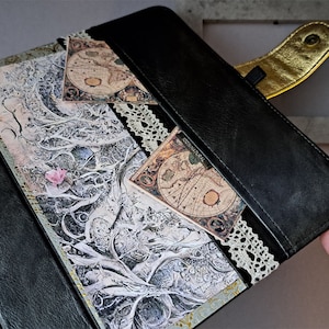 May include: A black leather journal with a gold clasp and lace trim. The cover features a vintage map design and a decorative paper with a tree branch pattern.