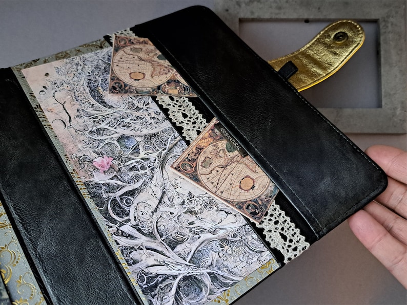 May include: A black leather journal with a gold clasp and lace trim. The cover features a vintage map design and a decorative paper with a tree branch pattern.