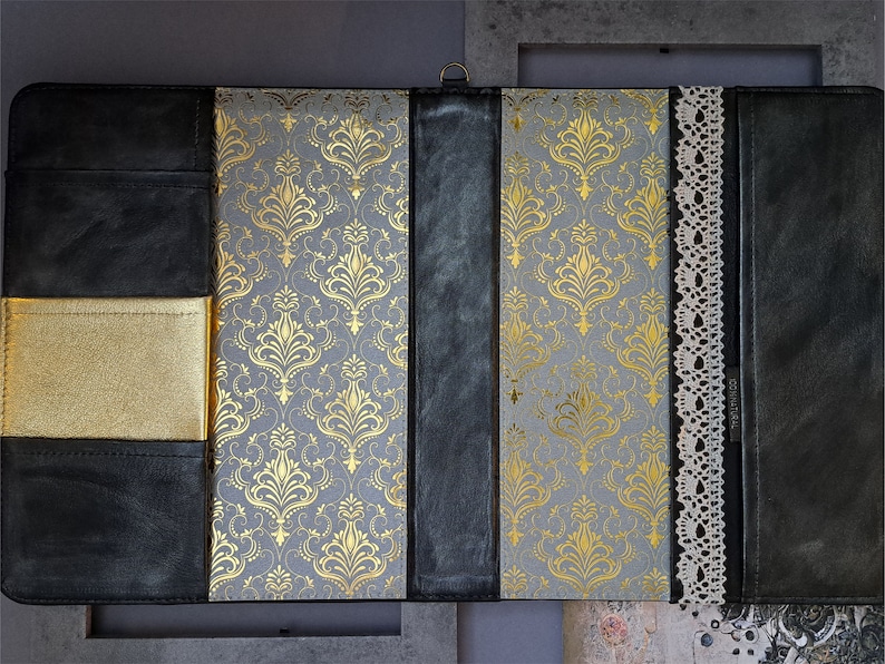 May include: A black leather journal with a gold patterned cover and a lace trim. The journal has a gold pocket on the front cover.
