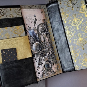 May include: A black leather journal with gold and gray patterned paper inserts. The journal has multiple pockets and a decorative closure.