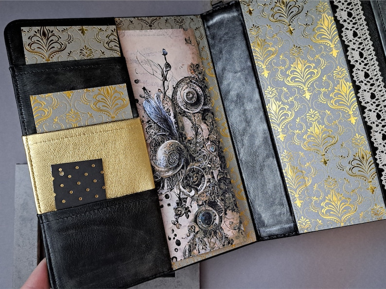 May include: A black leather journal with gold and gray patterned paper inserts. The journal has multiple pockets and a decorative closure.