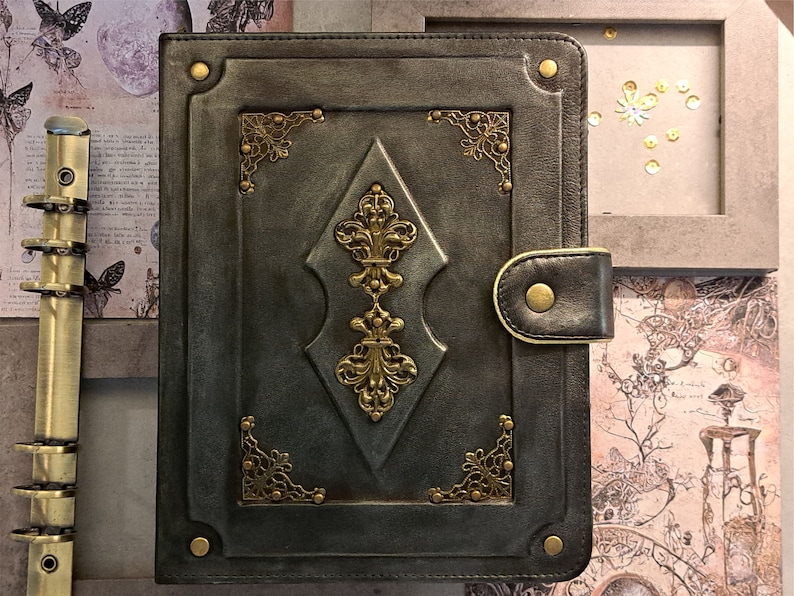 May include: A dark green leather-bound journal with gold accents and a decorative clasp. The journal has a vintage aesthetic and is perfect for writing, journaling, or sketching.