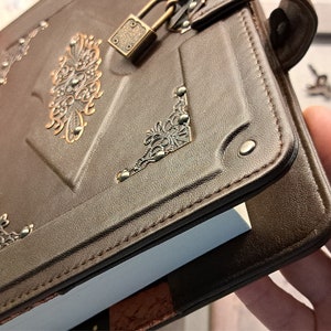 May include: A brown leather journal with a metal lock and decorative accents. The journal has a white page insert and is closed.