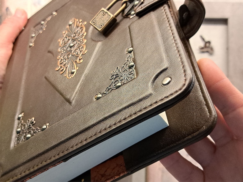 May include: A brown leather journal with a metal lock and decorative accents. The journal has a white page insert and is closed.