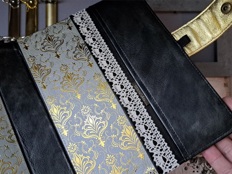 May include: A black leather journal with a gold and white damask pattern on the cover. The journal has a lace trim and the word "ORIGINAL" is embossed on the front.