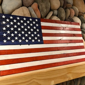 May include: A wooden American flag with red, white, and blue paint. The flag is made of individual planks of wood, and the stars are painted white on a blue background. The flag is hanging on a wooden mantle.