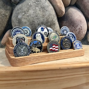 K&ouml;nnte beinhalten: Ein mehrstufiger Holzst&auml;nder zeigt eine Sammlung von bunten Challenge-M&uuml;nzen. Die M&uuml;nzen zeigen verschiedene Designs, darunter einen Totenkopf mit Knochen, eine amerikanische Flagge und eine Darstellung des Heiligen Michael.