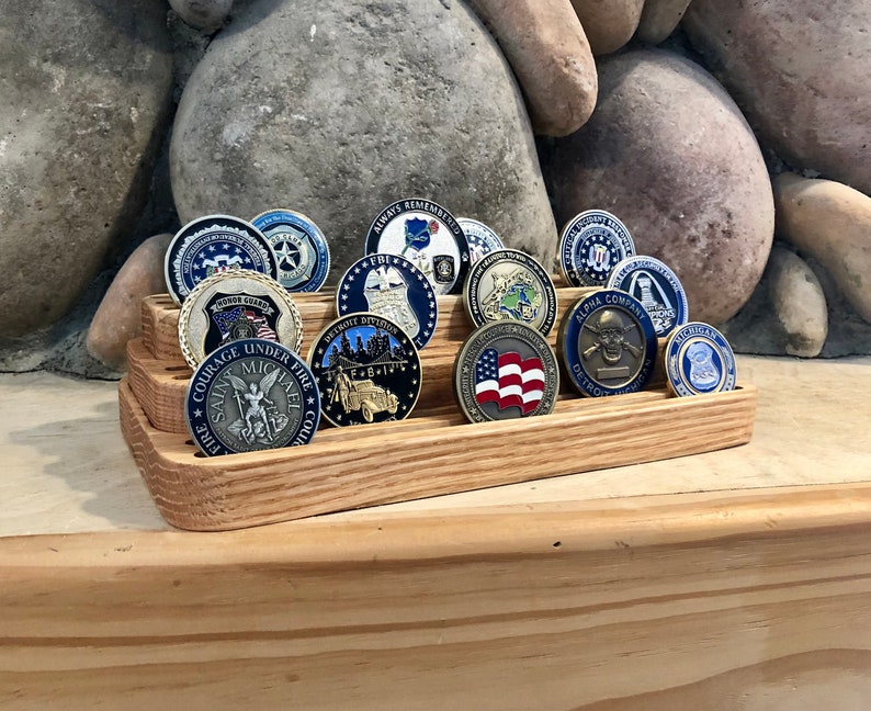 K&ouml;nnte beinhalten: Ein mehrstufiger Holzst&auml;nder zeigt eine Sammlung von bunten Challenge-M&uuml;nzen. Die M&uuml;nzen zeigen verschiedene Designs, darunter einen Totenkopf mit Knochen, eine amerikanische Flagge und eine Darstellung des Heiligen Michael.