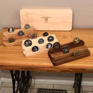 K&ouml;nnte beinhalten: Drei h&ouml;lzerne M&uuml;nzst&auml;nder mit Reihen von Schlitzen zum Aufbewahren von Challenge-M&uuml;nzen. Die St&auml;nder sind aus hellem Holz, dunklem Holz und einem nat&uuml;rlichen Holzfinish gefertigt. Die St&auml;nder stehen auf einem Holztisch mit einem N&auml;hmaschinensockel.