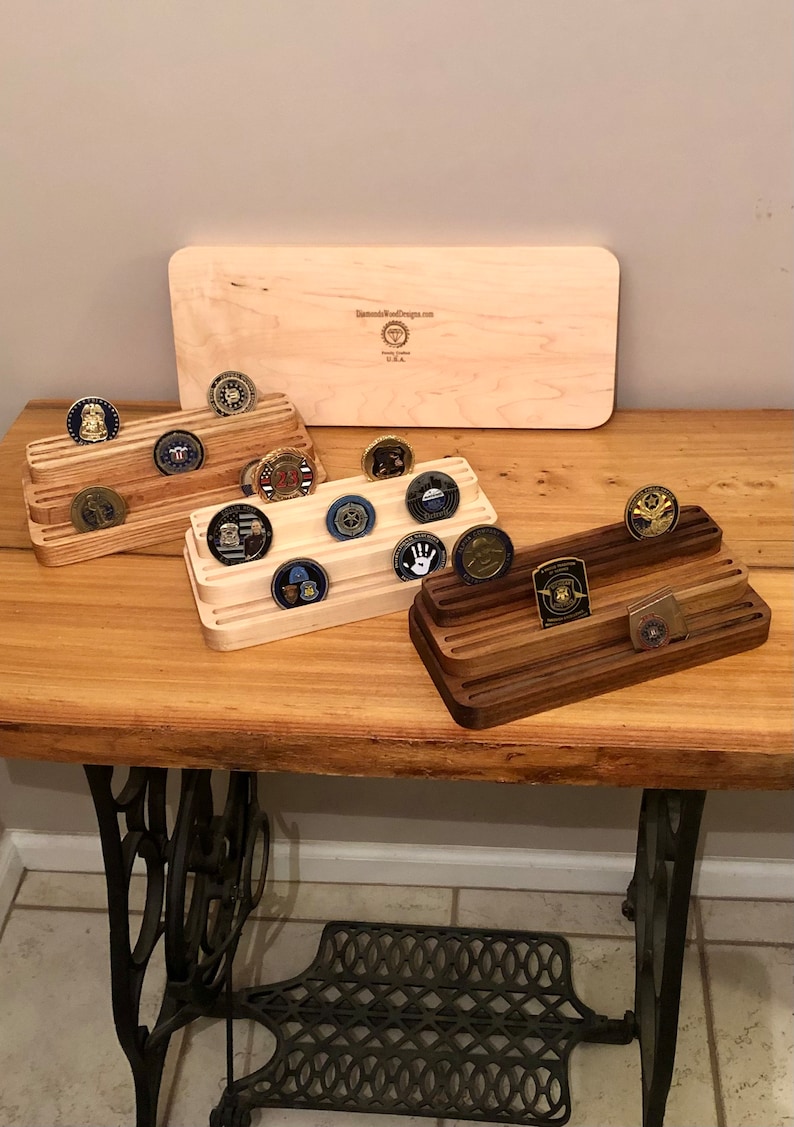 K&ouml;nnte beinhalten: Drei h&ouml;lzerne M&uuml;nzst&auml;nder mit Reihen von Schlitzen zum Aufbewahren von Challenge-M&uuml;nzen. Die St&auml;nder sind aus hellem Holz, dunklem Holz und einem nat&uuml;rlichen Holzfinish gefertigt. Die St&auml;nder stehen auf einem Holztisch mit einem N&auml;hmaschinensockel.