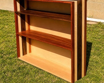 May include: A handcrafted wooden bookshelf with three shelves. The bookshelf features a combination of light and dark wood tones, with a natural finish. The shelves are made of a rich, dark wood, and the frame has a striped design.