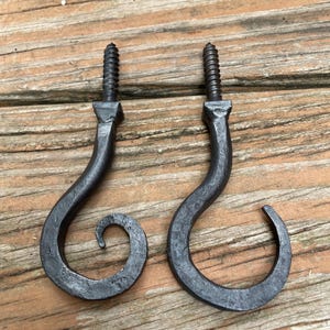 May include: Two dark gray metal hooks with a hammered texture and a curved, spiral design. Each hook features a threaded screw top for installation, with a tapered neck leading into a rounded, open-ended hook shape for hanging various items.
