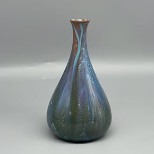 May include: A handcrafted ceramic vase with a teardrop shape. The vase features a blend of colours, including deep blues, greens, and hints of copper. The glaze creates a textured, iridescent effect. The vase is approximately 20 cm tall.