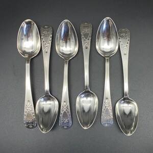 Può includere: Sei cucchiaini d'argento con manici decorati. Ogni cucchiaino presenta un design decorativo e l'iscrizione "1824" sul manico.