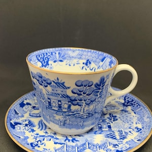 May include: A blue and white teacup and saucer set with a gold rim. The design features a Chinese landscape with a pagoda and trees.