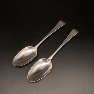 May include: Two silver spoons with oval bowls and long, slender handles. The spoons are polished and shiny.