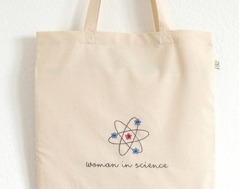 May include: A natural canvas tote bag with a black and white atom design and the text "woman in science".