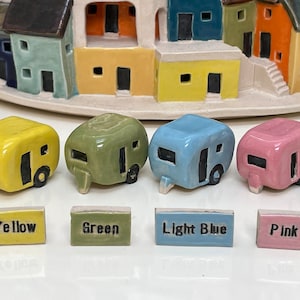 May include: Four miniature camper vans in yellow, green, light blue, and pink. Each camper van has a black window and door. Below each camper van is a small tile with the color name written in black.