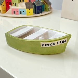 以下が含まれることがあります： 白の内装と側面に「Fink's Fun」と書かれた小さな緑色のセラミックボート