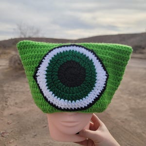 May include: Green crocheted beanie with a large white and green eye design.