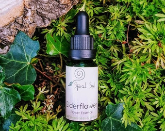 Op de afbeelding: Een klein, donkergroen glazen flesje met een zwarte druppelaar. Het flesje is gelabeld "Spiral Soul Elderflower Flower Essence for darkness & self-doubt". Het flesje staat op een bed van groen mos.