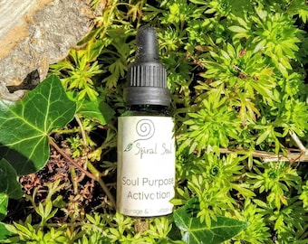 Puede incluir: Un pequeño frasco de vidrio verde oscuro con un gotero negro. El frasco está etiquetado con "Spiral Soul" y "Soul Purpose Activation". El frasco está sentado en un lecho de musgo verde.