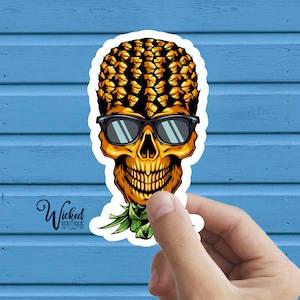 May include: A sticker featuring a skull with a pineapple for a head wearing sunglasses. The skull is smiling and has a green pineapple leaf sticking out of the top.