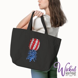 May include: A black tote bag with a red, white, and blue pineapple design. The pineapple is made up of stars and stripes.