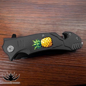 May include: A black pocket knife with a safety feature and a pixelated pineapple design on the blade.