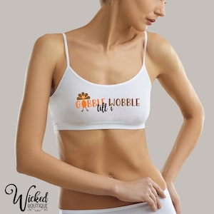 May include: White crop top with thin straps featuring the text "GOBBLE WOBBLE till I" in orange and brown. The design includes a cartoon turkey. The Wicked Boutique logo is visible at the bottom left.