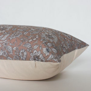 May include: A rectangular pillow with a floral print in shades of pink, white, and gray. The pillow has a zipper closure and a cream-colored back.