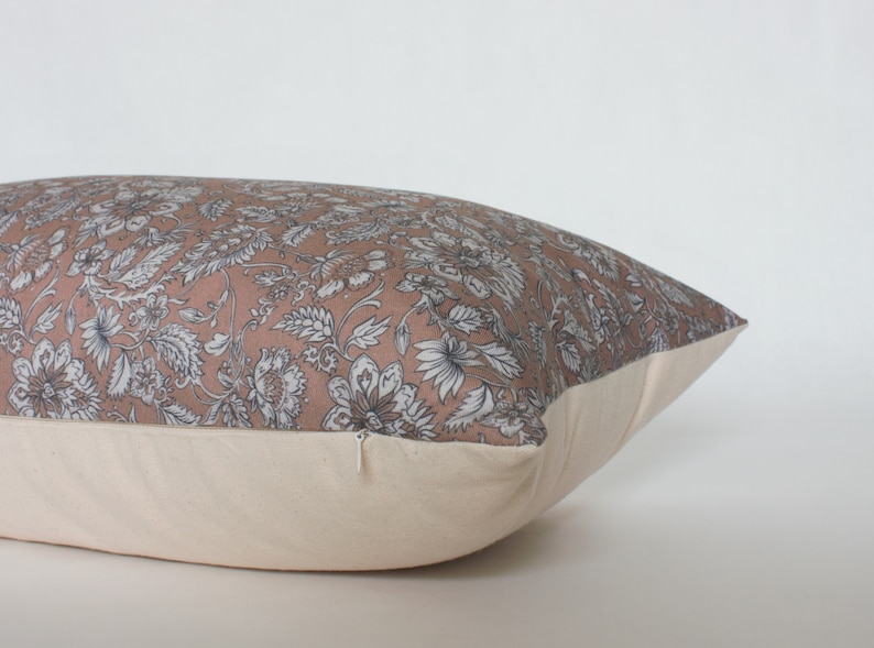 May include: A rectangular pillow with a floral print in shades of pink, white, and gray. The pillow has a zipper closure and a cream-colored back.